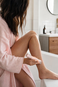 Mujer depilándose la pierna con la depiladora eléctrica en el baño